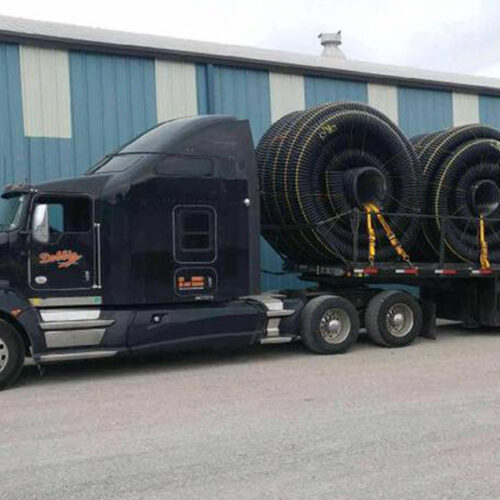 Freight truck with flatbed trailer hauling coiled hose